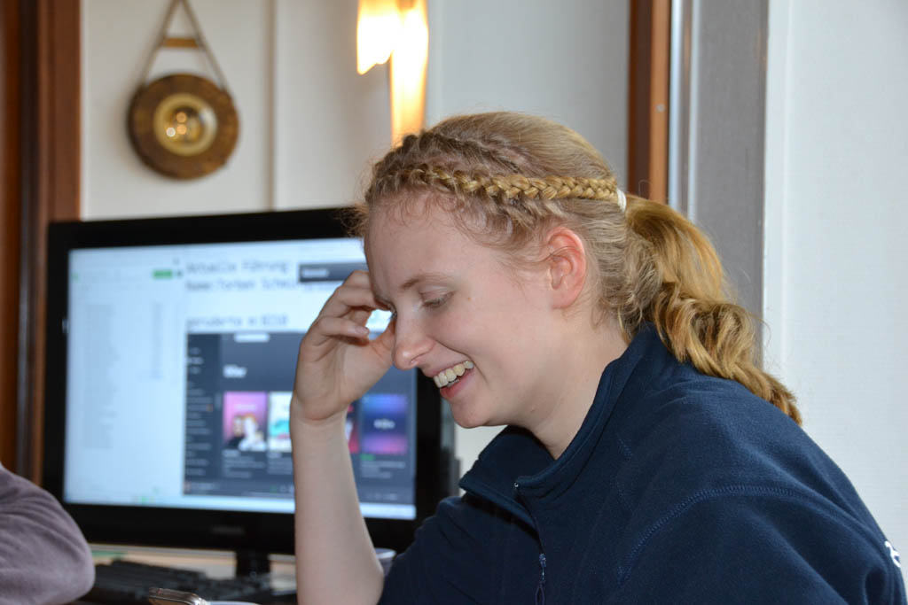 Eine junge Frau mit Zopfkranz im Haar lächelt, im Hintergrund ein PC-Monitor