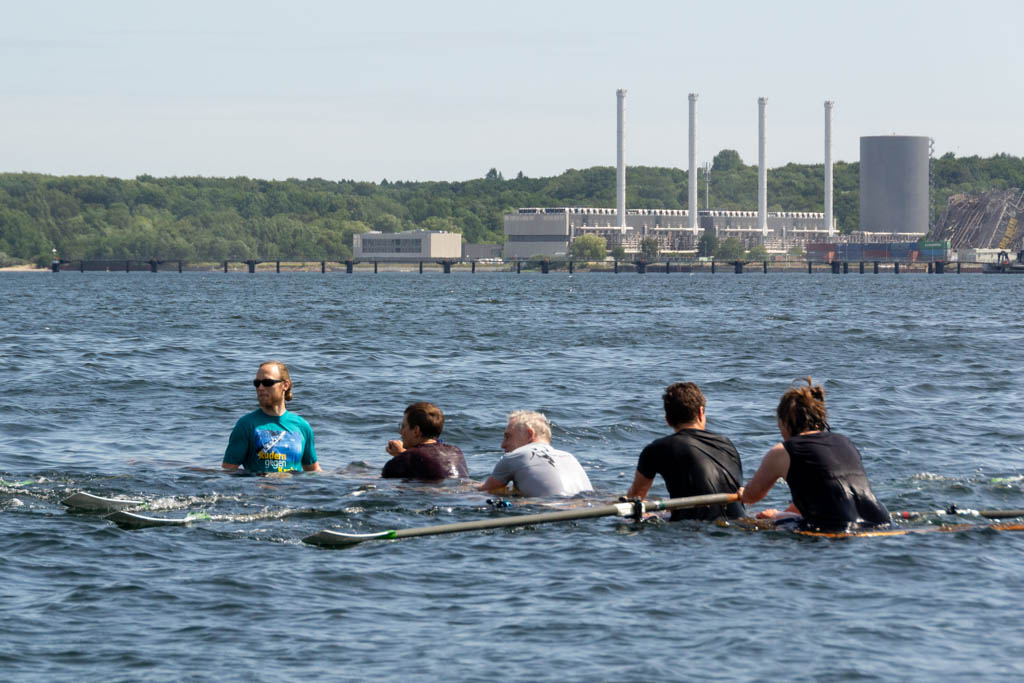 Ein Ruderboot ist in der Kieler Förde mit Wasser voll gelaufen. Fünf Personen sind mit ihrem Oberkörper über Wasser und versuchen zum Steg zu rudern.