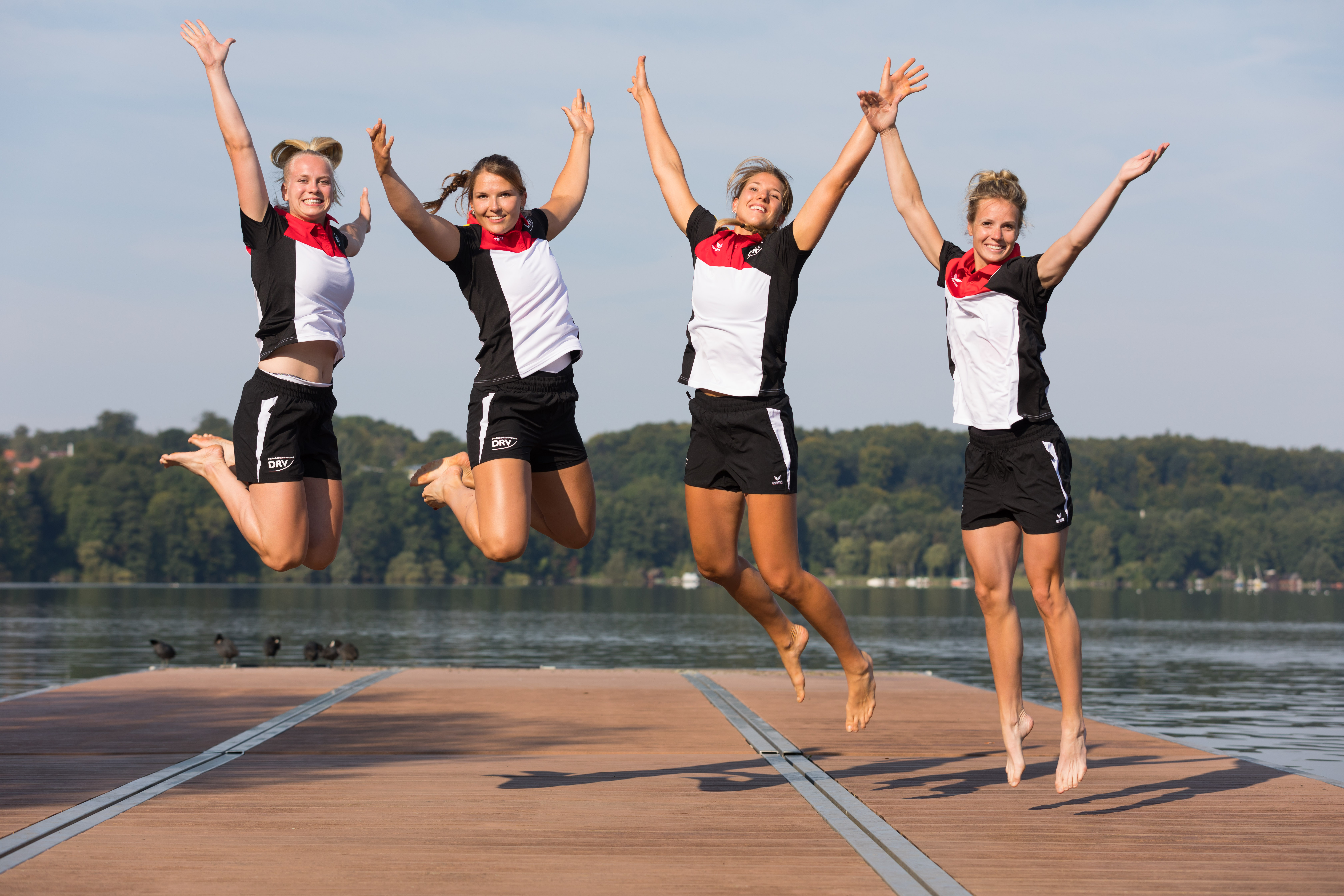 Vier junge Frauen in Sportkleidung springen auf einem Steg in die Höhe