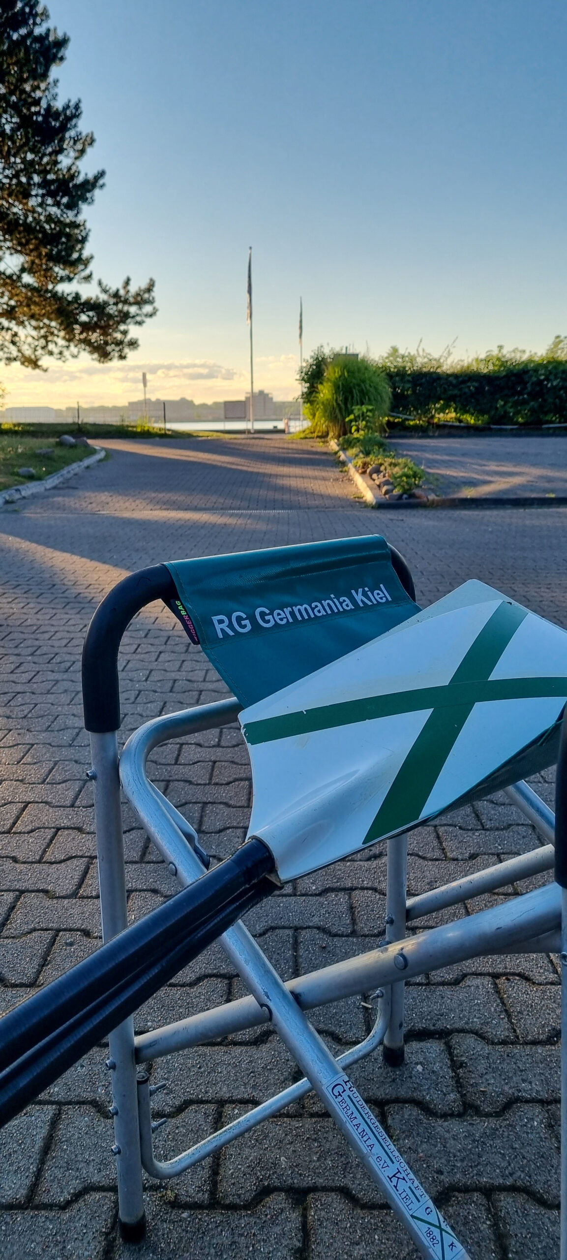 Ruderskull liegt auf einem Klappbock mit dem Schriftzug RG Germania Kiel - im Hintergrund schimmert die Kieler Förde