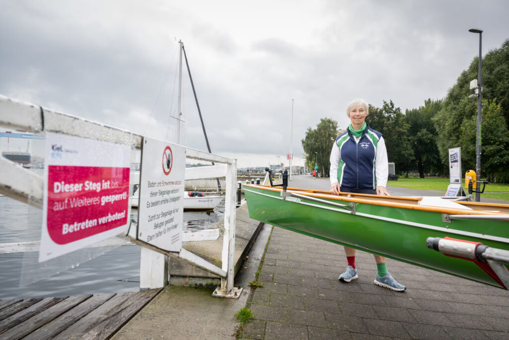 Ruderin steht mit Ihrem Ruderboot vor einem gesperrten Bootssteg.